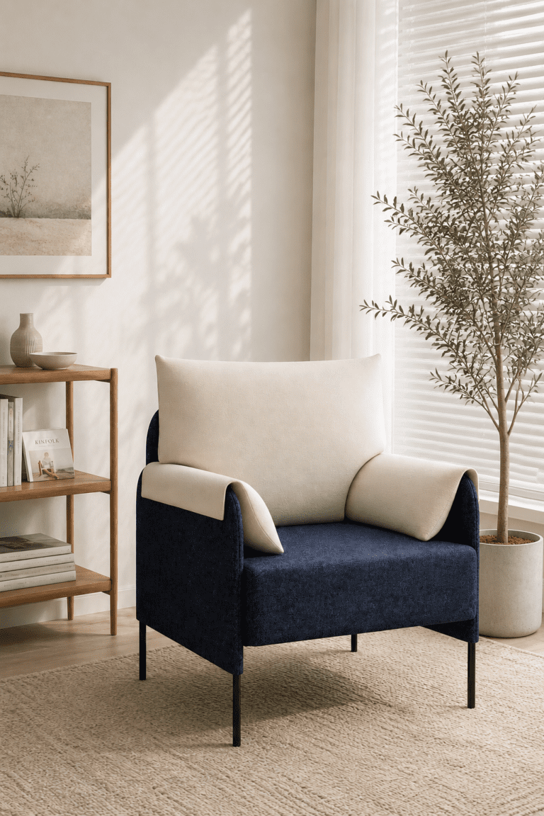 Cream and navy accent chair on a patterned rug beside indoor plants and bright white window blinds.